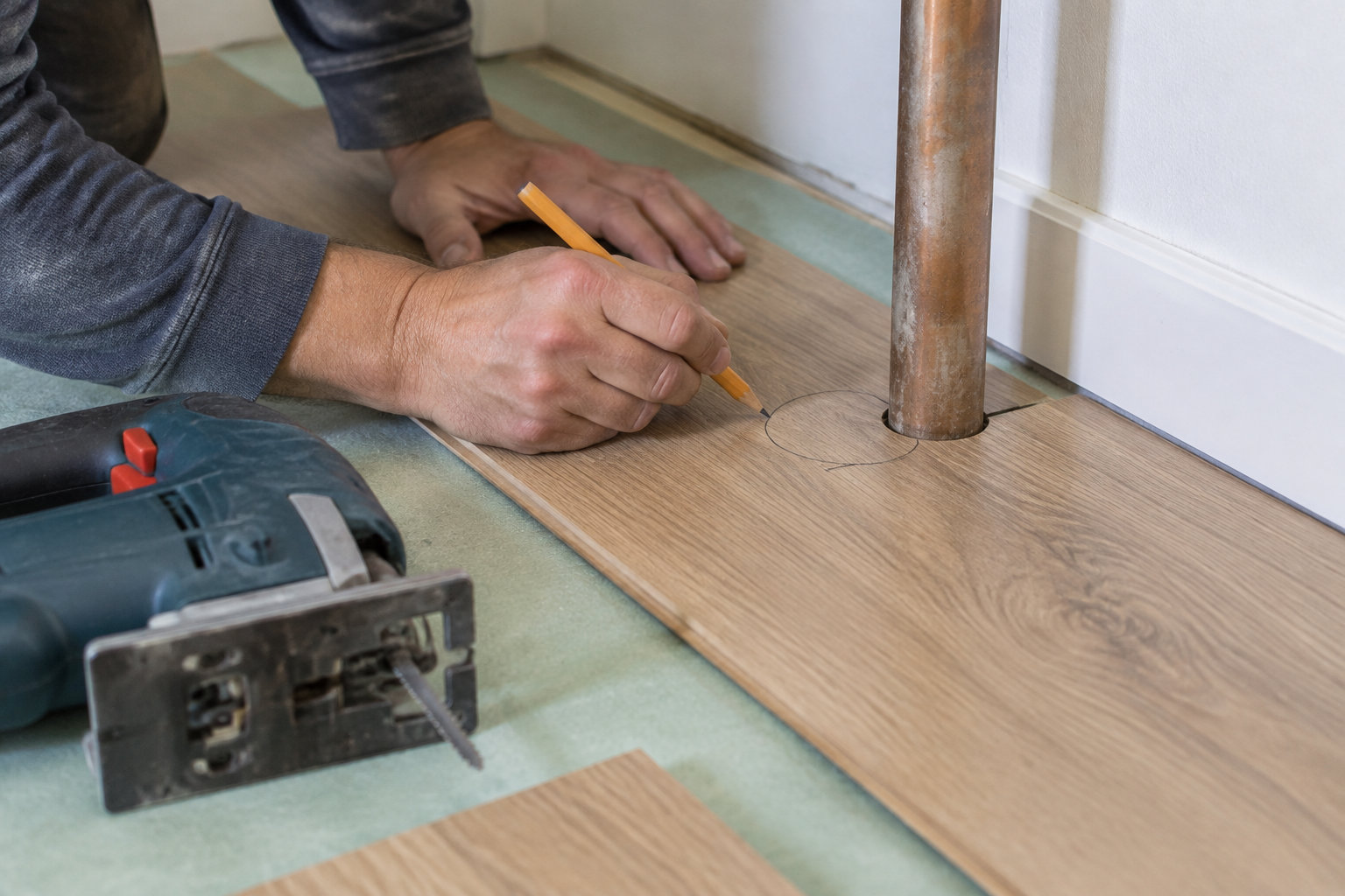 Une personne trace au crayon un cercle autour d’un tuyau sur une planche de bois, près d’une scie sauteuse.